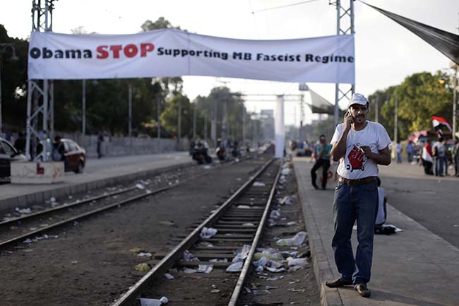 An opponent of Egypt's Islamist President Mohammed Morsi speaks on a mobile phone at a railway station decorated with a banner reading: Obama Stop supporting MB (Muslim Brotherhood) fascist regime in Cairo, Egypt, Monday, July 1, 2013. Hundreds of thousands thronged the streets of Cairo and cities around the country Sunday and marched on the presidential palace, filling a broad avenue for blocks, in an attempt to force out the Islamist president with the most massive protests Egypt has seen in 2¬Ω years of turmoil. (AP Photo/Hassan Ammar)