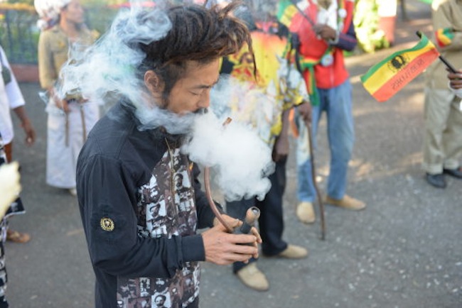 In this Feb. 6, 2013 photo, a Rastafarian named Bongho Jatusy smokes a pipe of marijuana outside a museum dedicated to the memory of late reggae icon Bob Marley in Kingston, Jamaica. While marijuana is still illegal in Jamaica, where it is known popularly as ¬ìganja,¬î increasingly vocal advocates say that Jamaica could give its struggling economy a boost by taking advantage of the fact the island is nearly as famous for its marijuana as it is for beaches, reggae music and world-beating sprinters. (AP Photo/David McFadden)