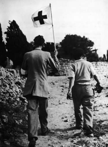 Swiss Jean Courvoisier, staff member of the Red Cross in Jerusalem, holds his organization's flag as he walks together with an unidentified colleague on no man's land in search for victims of the Jewish Arab conflict on May 10, 1948 in the Katamon outskirts of Jerusalem, Israel. Despite of the flag he was shot on twice by Arab snipers.