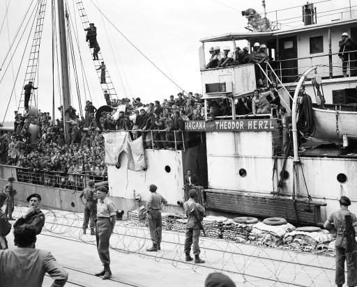 Jewish refugees, arriving on April 14, 1920 in Haifa, Palestine, aboard the Theodore Herzl. Some are carrying on their shoulders the bodies, in white shrouds, of two of their compatriots, who they say were slain when the Theodore Herzl was boarded by British personnel after unsuccessfully attempting to run the British Blockade.