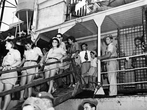 British soldier, armed with a sten gun on guard near the gangway, watches the young happy Jewish orphans as they leave the ship in the port of Haifa, Palestine, Aug. 21, 1947, where they will be bussed to Athlit for medical examination and then sent to their new homes and settlements. Five hundred orphans, the majority of whom lost their parents during World War II, were interned in Cyprus and brought to Palestine as part of the monthly immigration quota.