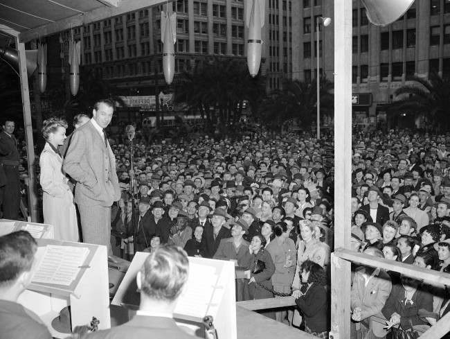Volunteer salesman Gary Cooper takes time out from work in a new movie to chalk up the highest record for selling Defense Bonds at the Defense House in Pershing Square in Los Angeles, California on Feb. 8, 1942, after making a stirring 15-minute speech, the longest of his public career. Cooper attracted the longest line of purchasers and sold more bonds than any motion picture star since the Defense House was opened, according to the Treasury Department. With him on the platform is lovely Virginia Gilmore of the films. (AP Photo)