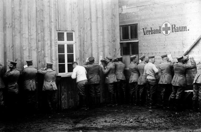 c1915: German soldiers, outside a Field Post Office, making use of a wall to write home from the Front.