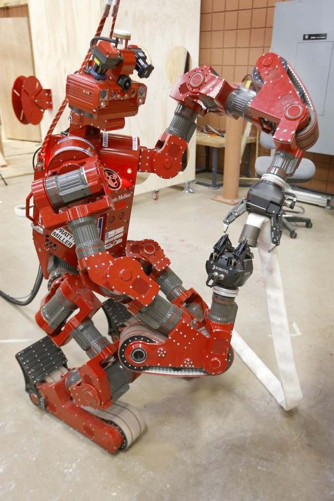 In this Wednesday, Dec. 11, 2013 photo, the CMU Highly Intelligent Mobile Platform robot, known as CHIMP, (CMU Highly Intelligent Mobile Platform) is put through some paces as it is switching the hold of a fire hose from one grasping unit to another at the National Robotics Engineering Center in Pittsburgh. Carnegie Mellon researchers are testing the new search-and-rescue robot that will compete in the U.S. Defense Department's upcoming national robotics competition in Florida. Competitors from other schools and companies will be vying for a $2 million U.S. Defense Department prize. (AP Photo/Keith Srakocic)