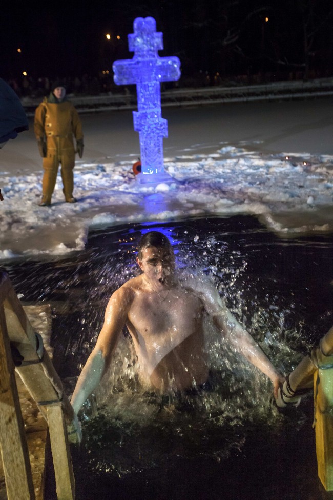 A Russian man emerges from the icy water in a pond to mark the Epiphany, as a lifeguard gets ready to help him, in Moscow, Russia, early Sunday, Jan. 19, 2014. 