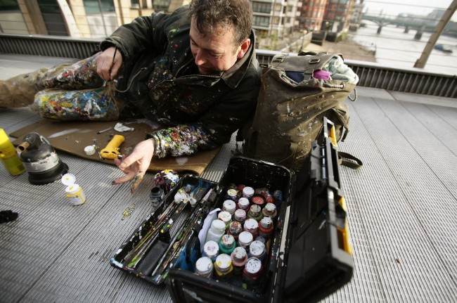 Artist Ben Wilson who paints art on discarded gum, and is also known as 'Chewing Gum Man', at work on the Millennium Bridge in London.
