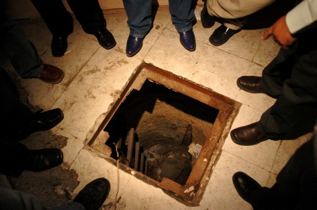 Mexican federal agents stand at the entrance to a hidden tunnel, presumably used to transport drugs from Mexico to the U.S., on Thursday, July 8, 2004 in Tijuana, Mexico. The tunnel, which starts in an abandoned house in Tijuana, crosses under the U.S. border wall. (AP Photo/David Maung)