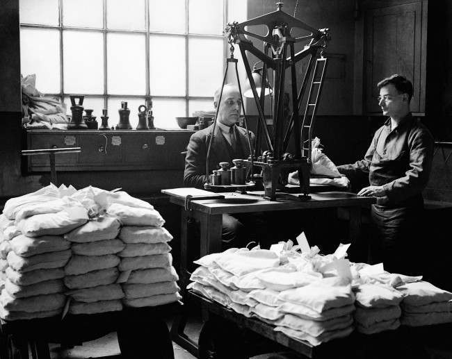 The Royal Mint - London - 1933 Workers weigh the finished coins into bags using the 'automatic weighing machine'.