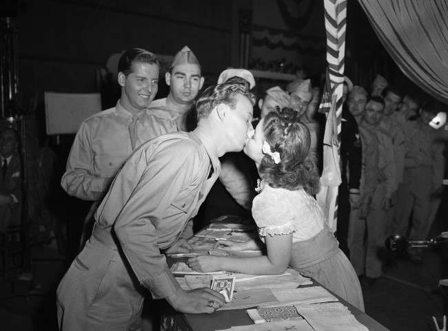 For the first time in her long movie career, Shirley Temple gets kissed in grown-up fashion by Jerry Shane, an ex-Marine from Grand Rapids, Mich., who plays a bit part in the movie called "Kiss and Tell," Jan. 19, 1945. Some observers at the historical occasion suspected that Shirley's performance was backed by a little previous necking experience, but Shirley wouldn't admit it. (AP Photo/Ira W. Guldner)