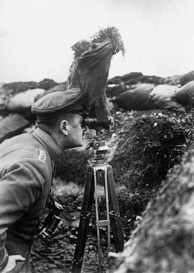 A German Army officer taking observations from a trench by means of a pair of periscope binoculars screened with sacking.