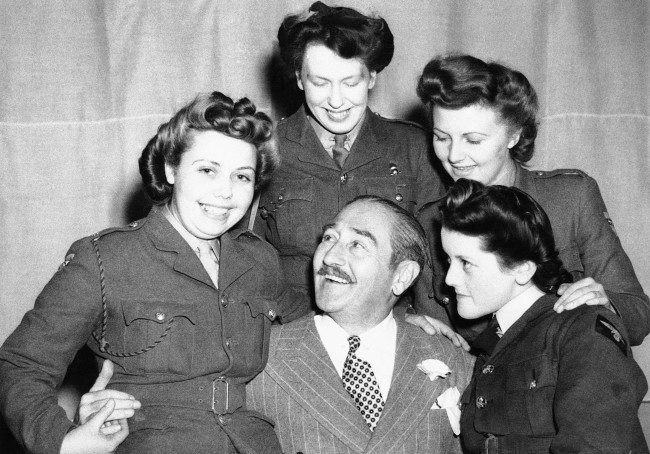 Adolphe Menjou, the famous film star, is seen making friends with three A.T.S. girls and A.W.A.A. girls at his first troop concert in this country June 14, 1943. (AP Photo)