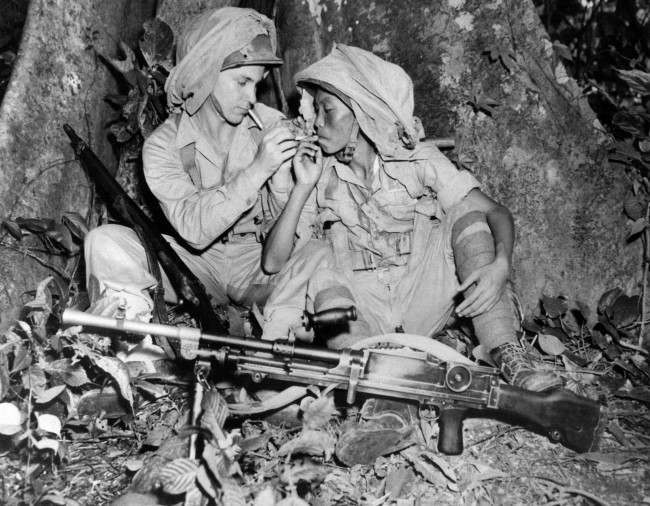 Corp. Rolf Krog, left, of St. Joseph, Mo., lights a cigarette for a Chinese soldier in the China-Burma-India theatre of operations on Oct. 14, 1943 where Chinese have been trained in use of American Army equipment for the past year. Mosquito netting in fastened to each helmet. 