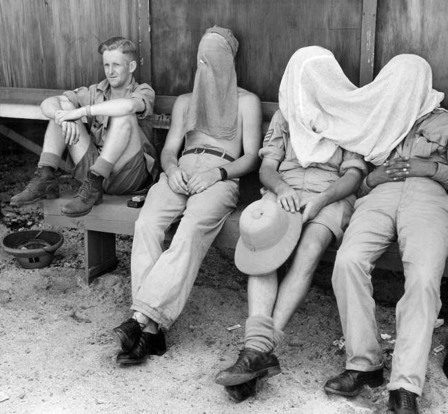 Protected by veils against the onslaught of the annoying and germ bearing-mosquito, three New Zealanders relax in the shade on Espiritu Santo on April 18, 1944, where they are receiving instruction in the operation of U.S. Navy planes. A comrade, scorning the netting, lets the mosquitoes fire away.