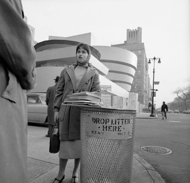 Resting her books on a New York waste basket industrial design student Christl Wilhelm says the building behind her has no warmth and no spirit, March 31, 1959. She'll get a lot of argument from devotees of architect Frank Lloyd Wright, whose works always seem to stir arguments. Wright designed the vat-shaped structure on upper Fifth Avenue. It is the Solomon R. Guggenheim Museum. 
