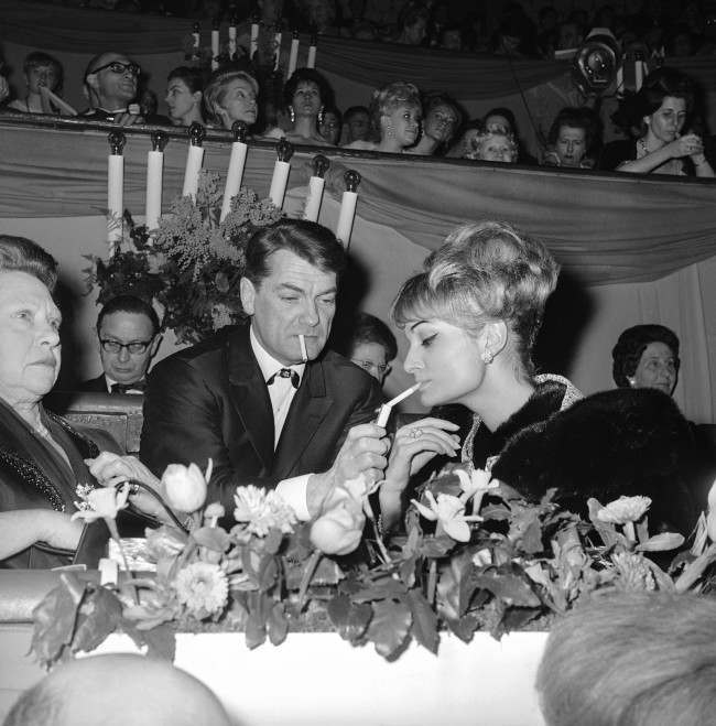 French actor Jean Marais, center, lights up the cigarette of Francoise Garbine at the Cirque d'Hiver (Winter Circus) on March 8, 1963 in Paris, France. Sitting at left is his mother. 