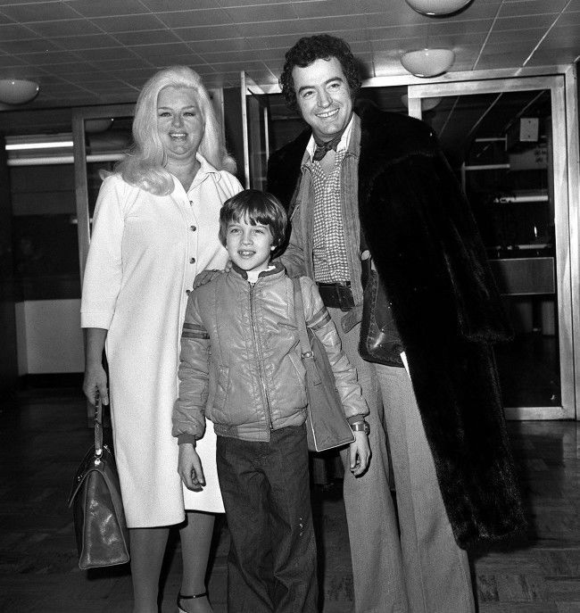 Off to Hollywood, California from London's Heathrow airport today, are actress Diana Dors, her husband, actor Alan Lake, and nine year old son Jason. Alan who feels the cold, wears one of Diana's own Christmas presents - a full length mink coat. In America, Miss Dors will visit her grown up sons and appear on TV chat shows. Ref #: PA.1244666  Date: 28/12/1978