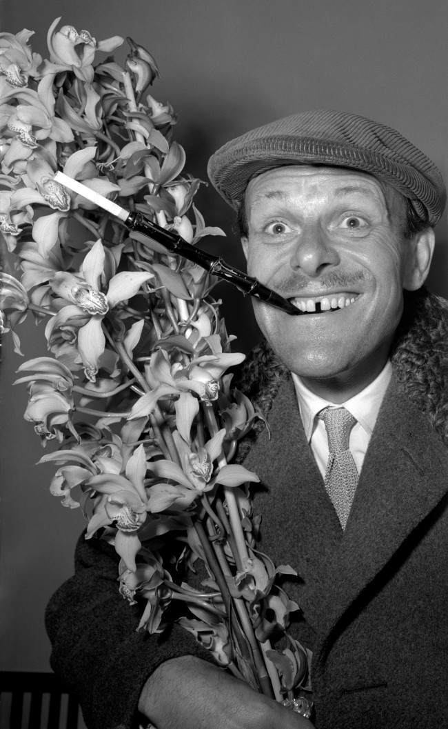 : TV's elegant comedian Terry-Thomas, who exhibits a distinctive sartorial style, returns from a holiday in Madeira sporting a cap and extended cigarette holder. He carries a bush of orchids for his wife. He is pictured at Southampton. Date: 25/03/1952