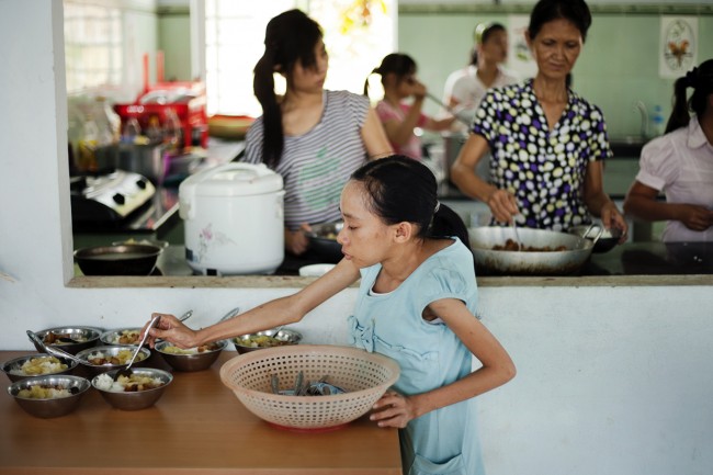 In this photo taken on Wednesday, Aug. 8, 2012, Ho Thi Lang, foreground, helps prepare lunch for other children at a rehabilitation center in Danang, Vietnam. The children were born with physical and mental disabilities that the center's director says were caused by their parents' exposure to the chemical dioxin in the defoliant Agent Orange. On Thursday, the U.S. for the first time will begin cleaning up leftover dioxin that was stored at the former military base that's now part of Danang's airport. 