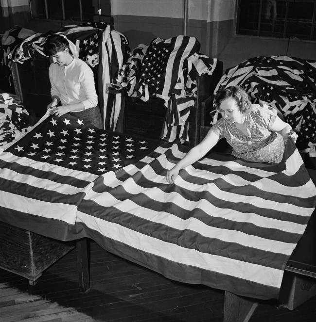 The new 49-star American flag is rolling off the assembly lines in ever increasing numbers and the Dettra plant, one of the largest, with a force of 240, is at work filling orders at Oaks, Penn., March 2, 1959. Judy Buse, left, and Mamie Myers check a completed flag for loose threads and other possible defects before shipment. 