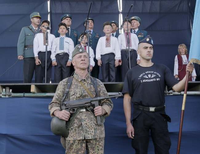 Two Ukrainians, one of them dressed in the SS Galychyna Division uniform, stand in guard of honor as children and SS Galychyna Division veterans sing during commemoration events in front of a monument to SS Galyhyna Division near the village of Yaseniv in western Ukraine on Sunday, July 21, 2013. Western Ukraine marks the 70th anniversary of creation of the SS Galychyna Division (the 14th Waffen Grenadier Division of the SS, 1st Ukrainian), a World War II German military formation initially made up of volunteers from the region of Galychyna with a Ukrainian ethnic background. Formed in 1943, it was largely destroyed in the battle of Brody, reformed, and saw action in Slovakia, Yugoslavia and Austria before surrendering to the Western Allies by 10 May 1945. The Galicia Division has been accused of committing war crimes in Norway in 1943; suppressing the Jewish Warsaw revolt in April-May, 1943; of suppressing the Polish Warsaw uprising of 1944; of fighting in May 1944 in Italy against the allies at Monte Cassino, other was crimes. However, in Western Ukraine it is largely seen as national heroes because they were fighting for Ukraines independence from the Soviet regime. 