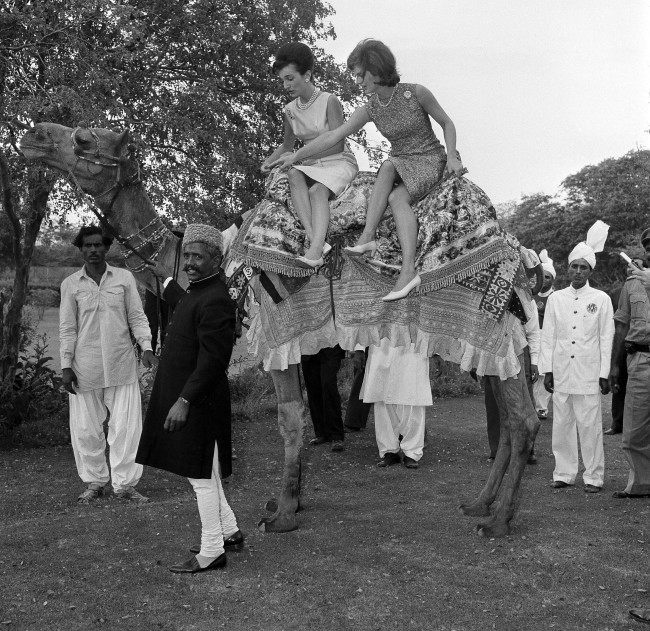 First lady Jacqueline Kennedy, right, goes for a camel ride, side saddle in a tight skirt in Karachi, Pakistan, March 25, 1962. Seated beside her is her sister Princess Lee Radziwill. Leading the camel is Bashir Ahmad, who visited the U.S. in 1961 as the guest of Vice President Johnson.