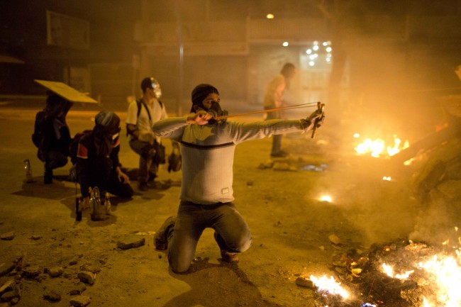 A masked demonstrator aims his slingshot loaded with a rock at Bolivarian National Guards during clashes in Caracas, Venezuela, Sunday, March 2, 2014. Since mid-February, anti-government activists have been protesting high inflation, shortages of food stuffs and medicine, and violent crime in a nation with the world's largest proven oil reserves.