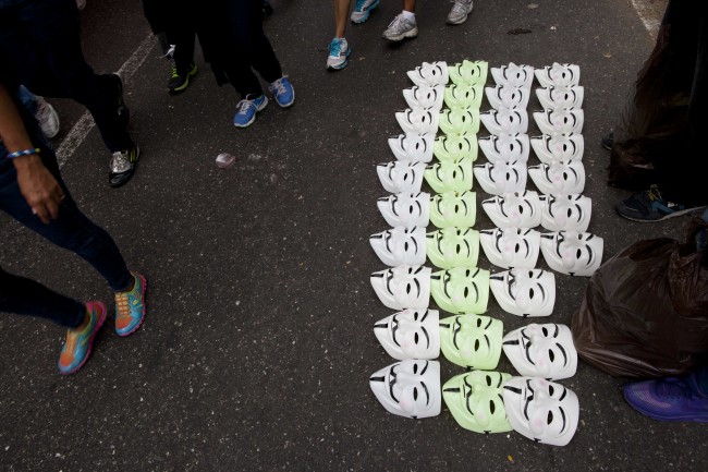 Demonstrators walk past Guy Fawkes masks for sale during an anti-government protest in Caracas, Venezuela, Sunday, March 2, 2014. Since mid-February, anti-government activists have been protesting high inflation, shortages of food stuffs and medicine, and violent crime in a nation with the world's largest proven oil reserves.