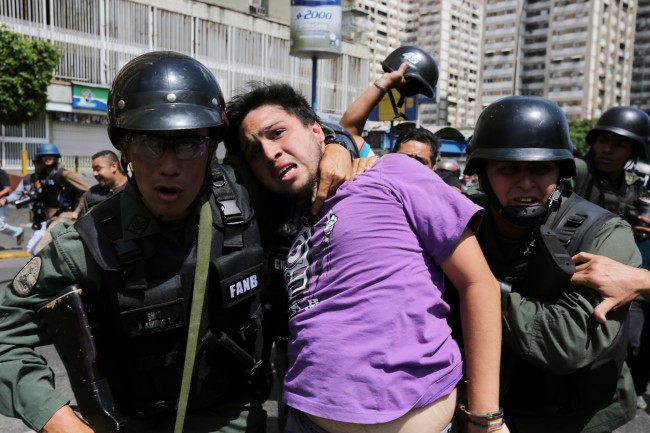 Bolivarian National Guards arrest an anti-government protester in handcuffs during clashes between motorcyclists and protesters in the Los Ruices neighborhood of Caracas, Venezuela, Thursday, March 6, 2014. Venezuelan officials say a National Guard member and a civilian were killed in the clash between residents and armed men who tried to remove a barricade placed by anti-government protesters. 