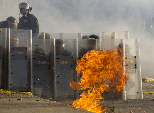 Bolivarian National Guard soldiers take cover behind their shields as a molotov cocktail lands during clashes near Plaza Altamira in Caracas, Venezuela, Sunday, March 16, 2014. Anti-government street protests by Venezuelans fed up with violent crime, shortages of basic items such as flour and cooking oil and high inflation have roiled Venezuela for more than a month. 