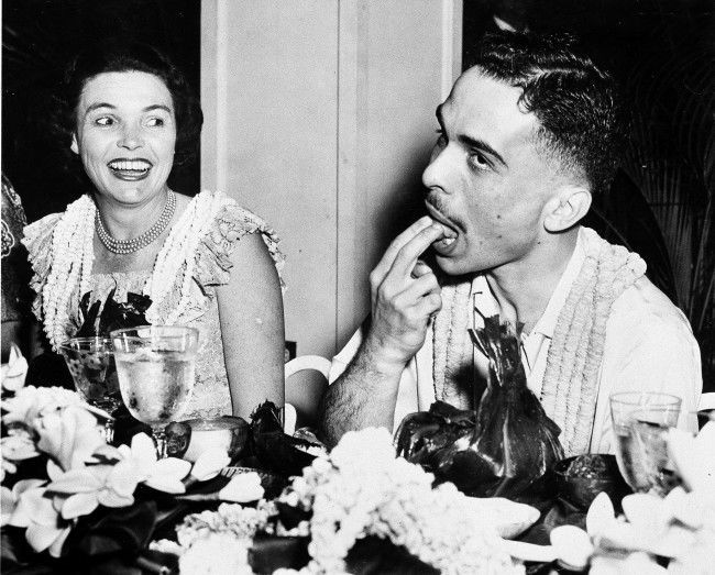 23-year-old King Hussein of Jordan tries a native Hawaiian dish at a feast given by Gov. William F. Quinn, as the governor's wife, Nancy, looks on. Hawaii, March. 19, 1959. 