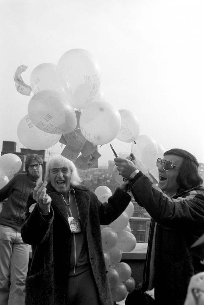 (L-R) Radio One disc jockeys Jimmy Savile and Alan Freeman threaten to burst the balloons which were to be launched from the roof of Broadcasting House to celebrate the fifth anniversary of the station Date: 29/09/1972 