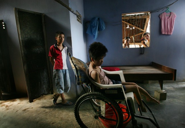 **Neighborhood children look through a window at Tran Thi Le Huyen, 23, sitting in a wheelchair in her family home in Danang, Vietnam in this May 21, 2007, file photo. The young woman has been listed by the Vietnamese government as a victim of Agent Orange contamination. Her family once lived near the highly contaminated Danang Airbase and her father was a driver for the US-backed south Vietnamese government during the war. Her family receives a small stipend and her wheelchair from the government. 