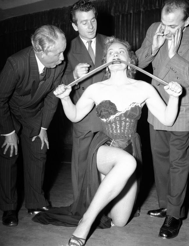 British strong woman, Joan Rhodes, demonstrates her strength and prowess by bending and iron bar with her bare hands and teeth for three interested men during her night club act Dusseldorf, Germany, Nov. 5, 1952. In Dec. 1955, Joan lifted comedian Bob Hope to her shoulders when Hope was in Iceland entertaining U.S. forces stationed there. Hope slipped from her grasp, hit the floor head-first and sustained a cut nose and injured neck. The following day he appeared on a British television show from London, after visiting a London doctor.