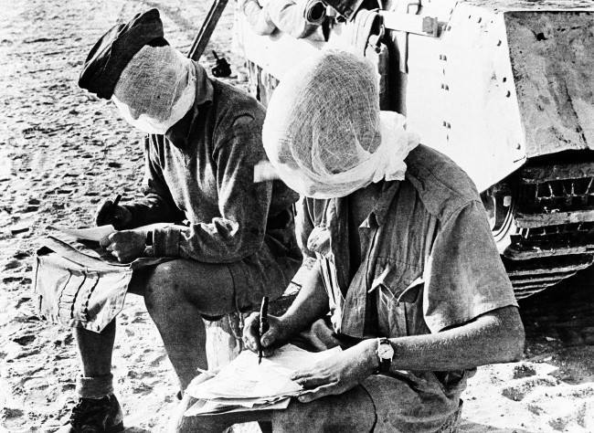 Members of a tank crew in the British forces in the Western Desert, in Egypt on Oct. 4, 1942, have to fight flies when they are not fighting the enemy. Soldiers writing home before a day's patrol wear mosquito netting masks.