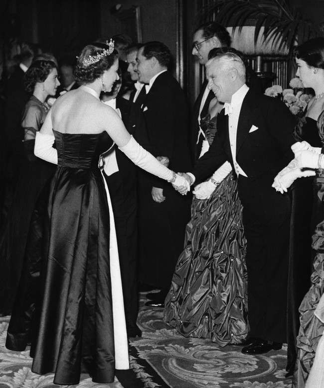 Queen Elizabeth II shakes hands with actor Charles Chaplin during meeting in Empire Theatre, London, for the Royal Film Performance, a benefit performance to aid the Cinematograph Trade Benevolent Fund. At left in background is Princess Margaret and at extreme right is Mrs. Oona Chaplin. Others are not identified. The movie shown was "Because You're Mine," marking first time that a musical from Hollywood had been chosen for this top British movie event. Chaplin, who was in London for recent premiere of his own new film, made a short appearance during hour-long stage show accompanying the movie presentation. Date: 27/10/1952