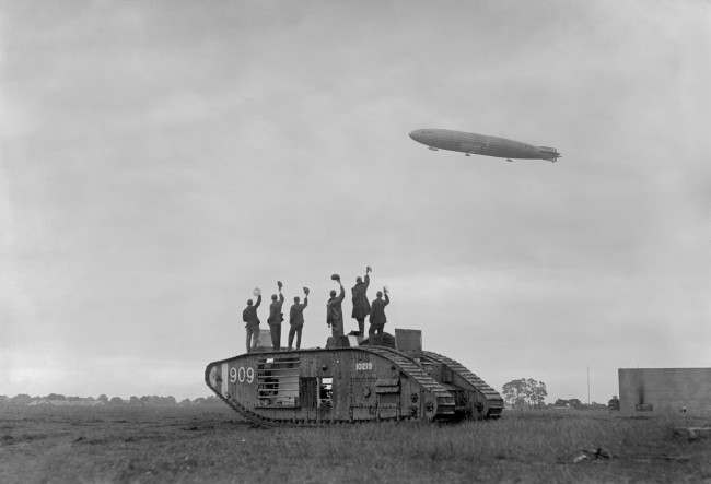 The Royal Navy Airship R34, returning from America to the aerodrome at Pulham, Norfolk, is cheered by British soldiers standing on a British Mark V tank. This was the first East-West crossing of the Atlantic and was done just two weeks after Alcock and Brown's first ever trans-Atlantic flight. Date: 13/07/1919
