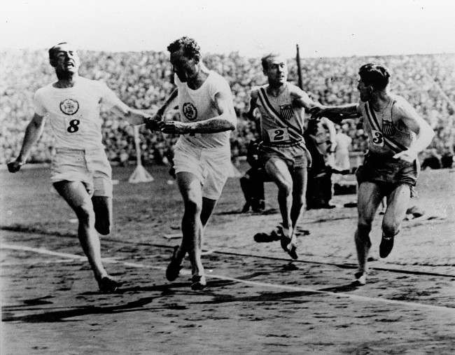 John Rinkel of Britain passes the baton to teammate Roger Leigh-Wood while American Taylor passes the baton to Raymond Barbuti during a meet between the U.S. and British Olympic relay teams at Stamford Bridge, England August 20, 1928. The U.S. team won the relay, setting the one-mile mark of 3 minutes, 13 2/5 seconds. 