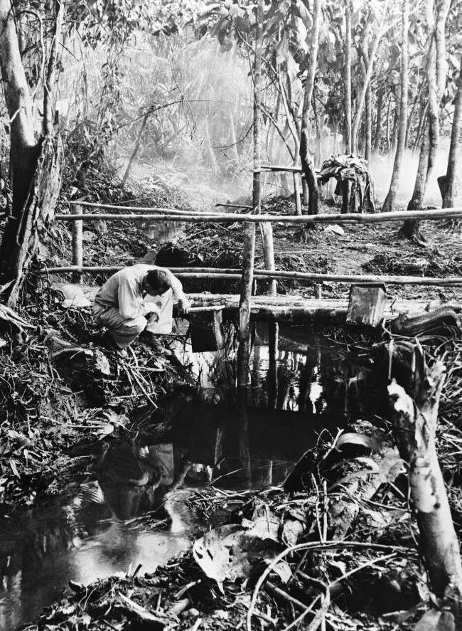 A U.S. soldier checks the oil supply in a drip can suspended from a foot bridge by Malaria control experts near a U.S. Army camp on South West Pacific Island of New Guinea, on August 26, 1944. Oil dripping from the can coats the surface of the sluggish stream and kills the larvae of Malaria-bearing mosquitoes.