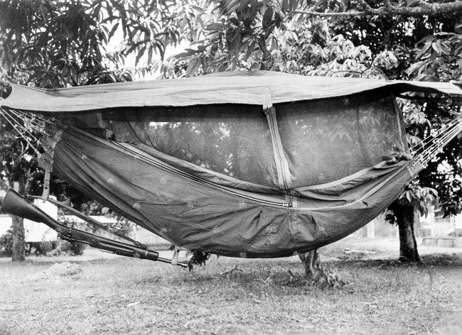 U.S. troops engaged in jungle maneuvers in Panama, August 5, 1942, have two methods of sleeping -- in a canopy-covered hammock (above) suspended from trees or on the ground (below) covered by cloth for protection against insects. Note rifle suspended from hammock. 