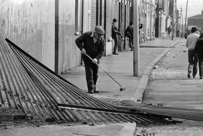 An old man sweeps broken glass outside his home, as a British army patrols a street in the Catholic Falls Road area of Belfast, Northern Ireland on May 6, 1981. After almost 36 hours of sporadic rioting, Belfast was quiet on Wednesday, following the death of IRA hunger striker Bobby Sands.