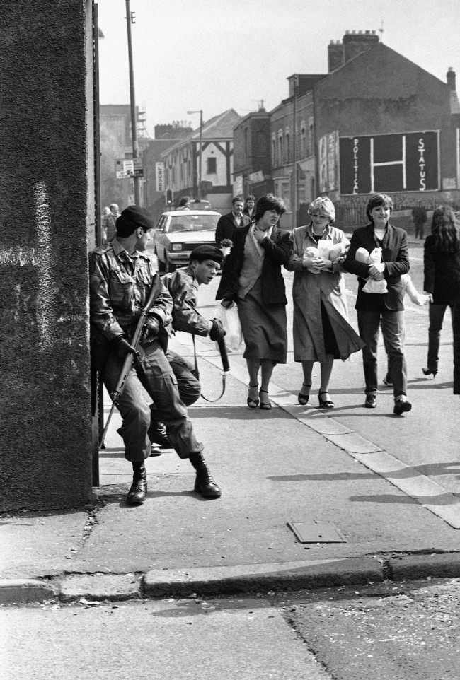 Three young girls stroll along a Belfast street, while two British soldiers of the Royal Fusiliers keep watch for snipers, after a spate of rioting in Belfast, Northern Ireland on May 5, 1981. Although rioters took to the streets in the early hours of the morning, following the death of IRA hunger striker Bobby Sands, much of the city had returned to normal by dawn. (AP Photo/Peter Kemp) Ref #: PA.10427042  Date: 05/05/1981