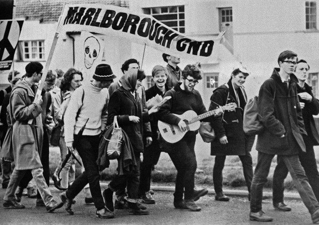 Teenagers in jeans, sweaters and duffle coats march to the accompaniment of a guitar as the 10,000 ban-the-bomb marchers leave Reading, Berkshire on April 21, 1952, on the second leg of their protest march from Aldermaston to London. They are marching under a banner reading ÂMarlborough CNDÂ (Campaign for Nuclear Disarmament).