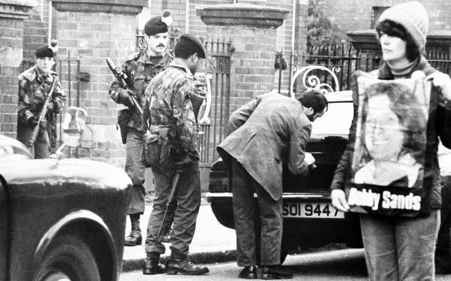 A protestor supporting the IRA hunger strikers stands in the center of the Catholic Falls road in Belfast on Friday, May 1, 1981, as troops of the royal fusiliers check cars at a roadblock. Tension remained high in Belfast, in anticipation of the death of IRA hunger striker Bobby Sands. (AP Photo/Peter Kemp) 