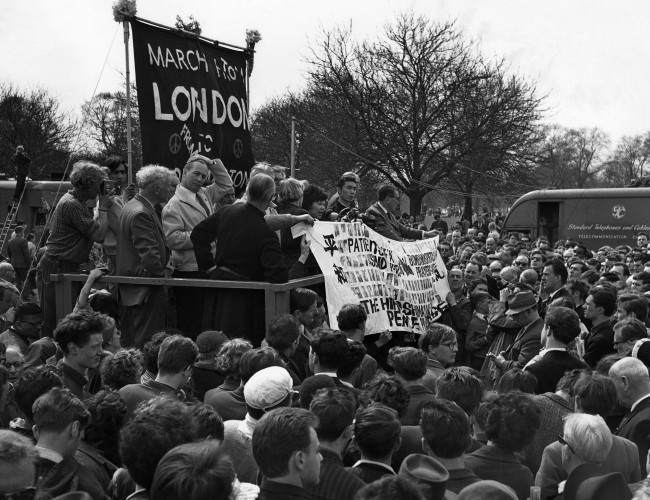 Two survivors of the Hiroshima atomic bomb hold up a banner as they join leaders of the Easter Ban-the-Bomb march on the dais in LondonÃ­s Hyde Park on April 23, 1962, at the mass rally climaxing the 50-mile march from Aldermaston. They are Miyoko Matsubara, a 29-year-old nurse, and Hirosama Hanabusa, 18, a law student. In black at near end of dais is Canon John Collins of St. PaulÃ­s Cathedral, chairman of the campaign for nuclear disarmament. 