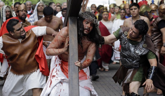Jose Nina, center, is whipped as he carries a cross playing the part of Jesus in a passion play and procession, Friday, April 18, 2014, in downtown San Antonio.