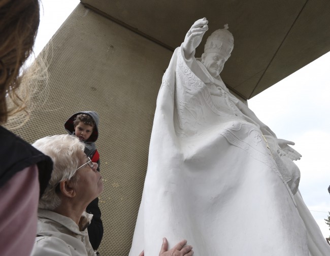 A faithful touches the statue of John XXIII while the canonization of Pope John XXIII and Pope John Paul II was taking place at the Vatican, at the parish church in Sotto il Monte Giovanni XXIII, northern Italy, the town of John XXIII