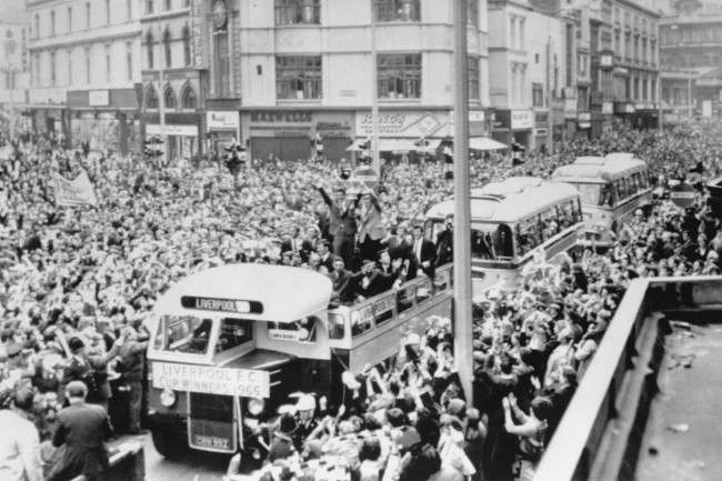 Displaying the FA Cup to the wildly cheering crowds, the Liverpool FC players are seen on their triumphal drive in an open top coach to the Town Hall from Lime Street Station for a civic reception on their return to Liverpool after beating Leeds Utd in the Cup Final at Wembley. Crowds estimated between 200,000 and 250,000 gave them a tumultuous welcome. The excited fans burst through the barriers and there were hundreds of casualties.