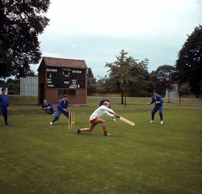 England's Bobby Charlton (white shirt) wafts his bat at the ball, watched by (l-r) Terry Paine, Bobby Moore, Martin Peters, Gerry Byrne and Peter Bonetti, as the England squad relax with a game of cricket during a training session at Roehampton Ref #: PA.2219404  Date: 15/07/1966