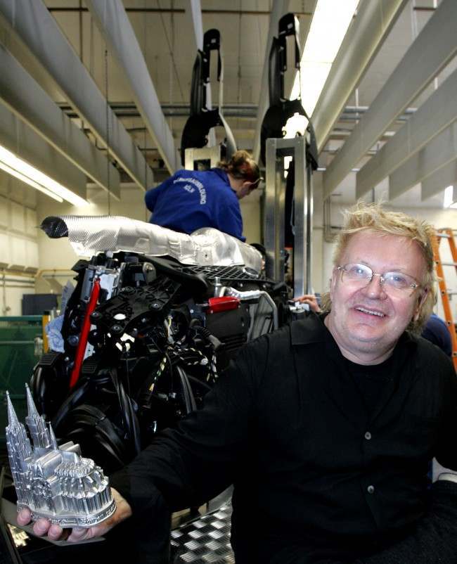 German performance artist HA Schult, right, holds a small model of the famous Cologne Cathedral, which he along with engineers and trainees of the Ford company rebuilds by assembling car fittings in Cologne, Germany, Tuesday, March 21, 2006. The sculpture, seen being assembled in background, will be auctioned to raise money for victims orphaned by the Sept. 11 terrorist attacks. The auction will be held in New York at the end of 2006. 