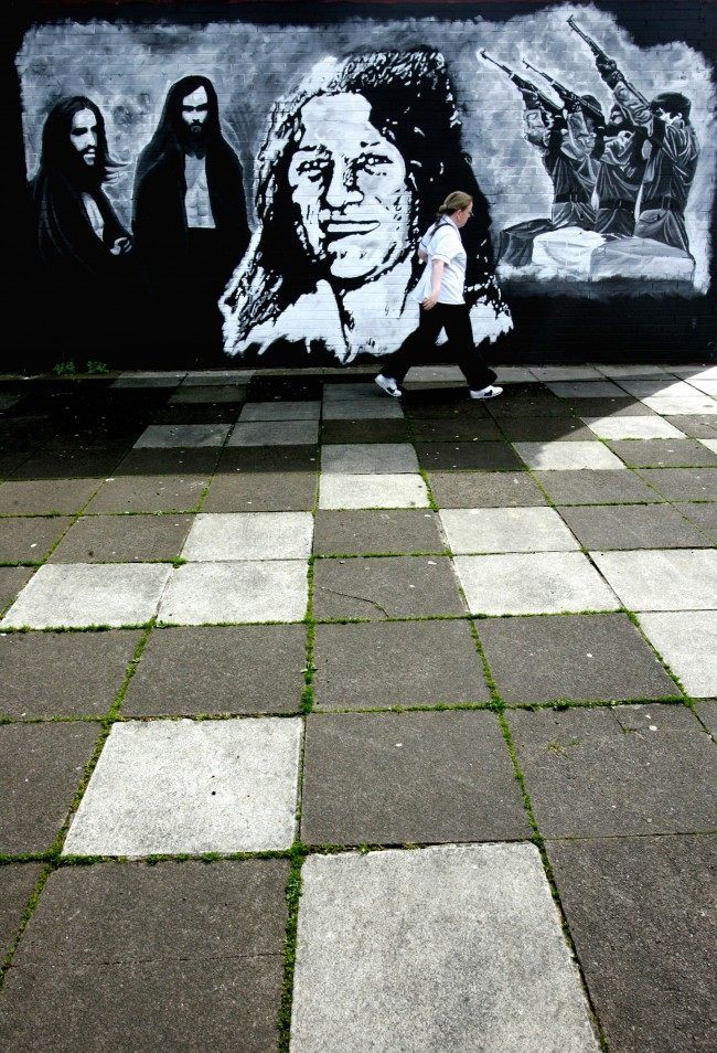 A woman passes a wall mural depicting Bobby Sands, at centre, commemorating the IRA hunger stikers in West Belfast, Northern Ireland, Friday, May, 5, 2006. 